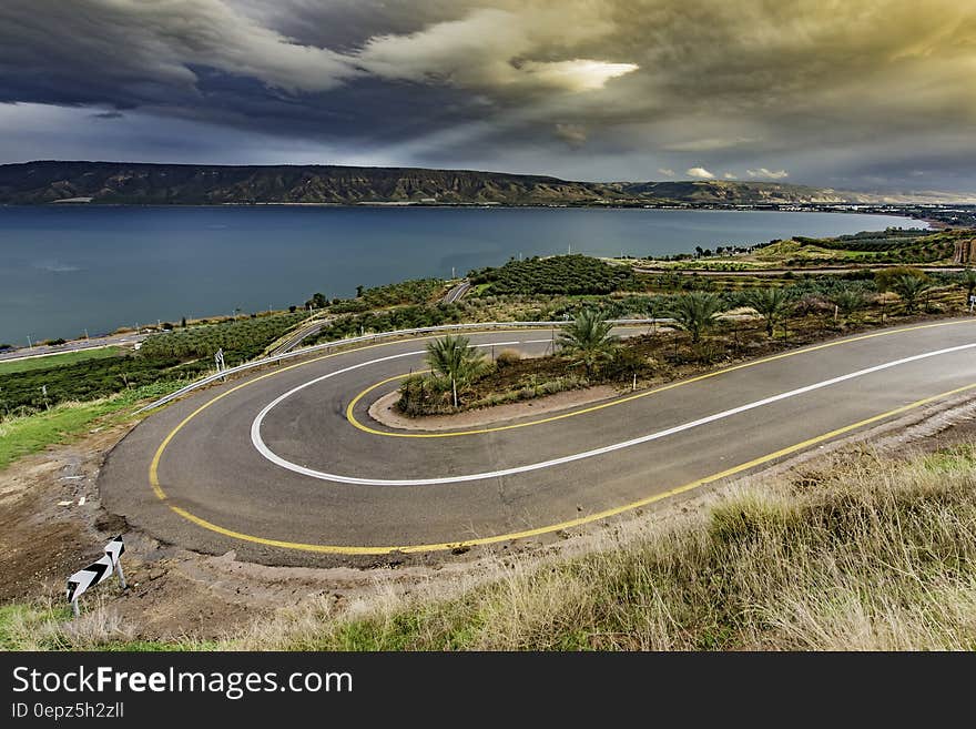 Curve Asphalt Road Near Blue Sea Under Gray Sky