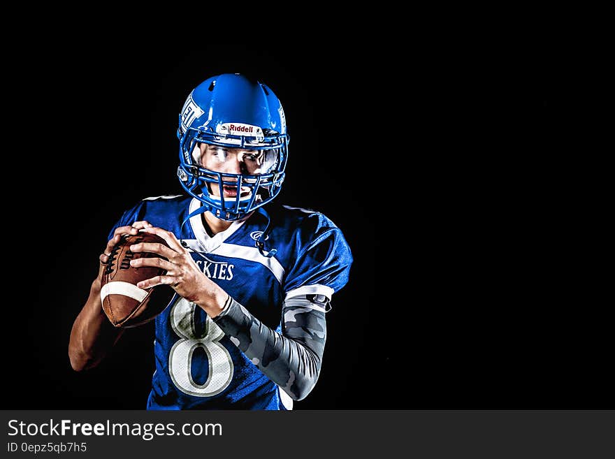 Man Holding Football and Football Uniform in Black Background