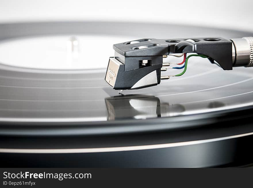 Long playing vinyl record on turntable with closeup of needle on the audio tracks and colored wires connecting to it (piezoelectric sensor).