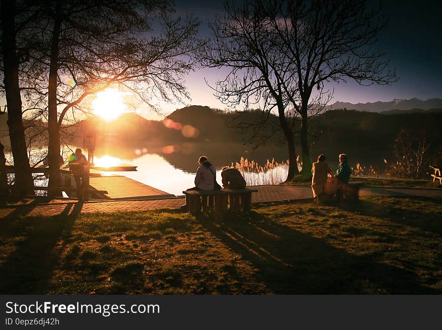 Couples sitting on wooden benches watching the golden sunrise over a lake and distant mountains and forests. Couples sitting on wooden benches watching the golden sunrise over a lake and distant mountains and forests.