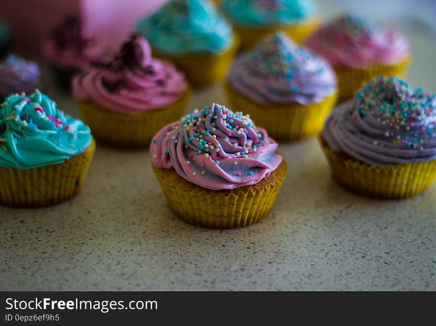 Closeup of cupcakes and selective focus with purple, blue and green icing decorated with sprinkles, on a speckled granite kitchen surface. Closeup of cupcakes and selective focus with purple, blue and green icing decorated with sprinkles, on a speckled granite kitchen surface.