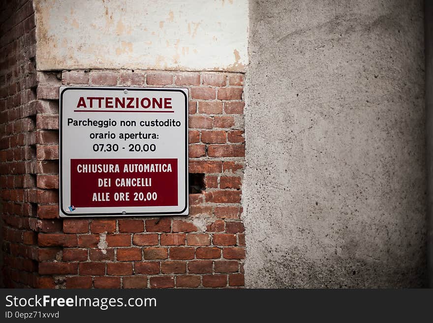 A sign on brick wall warning about the parking area being unguarded during the day. A sign on brick wall warning about the parking area being unguarded during the day.