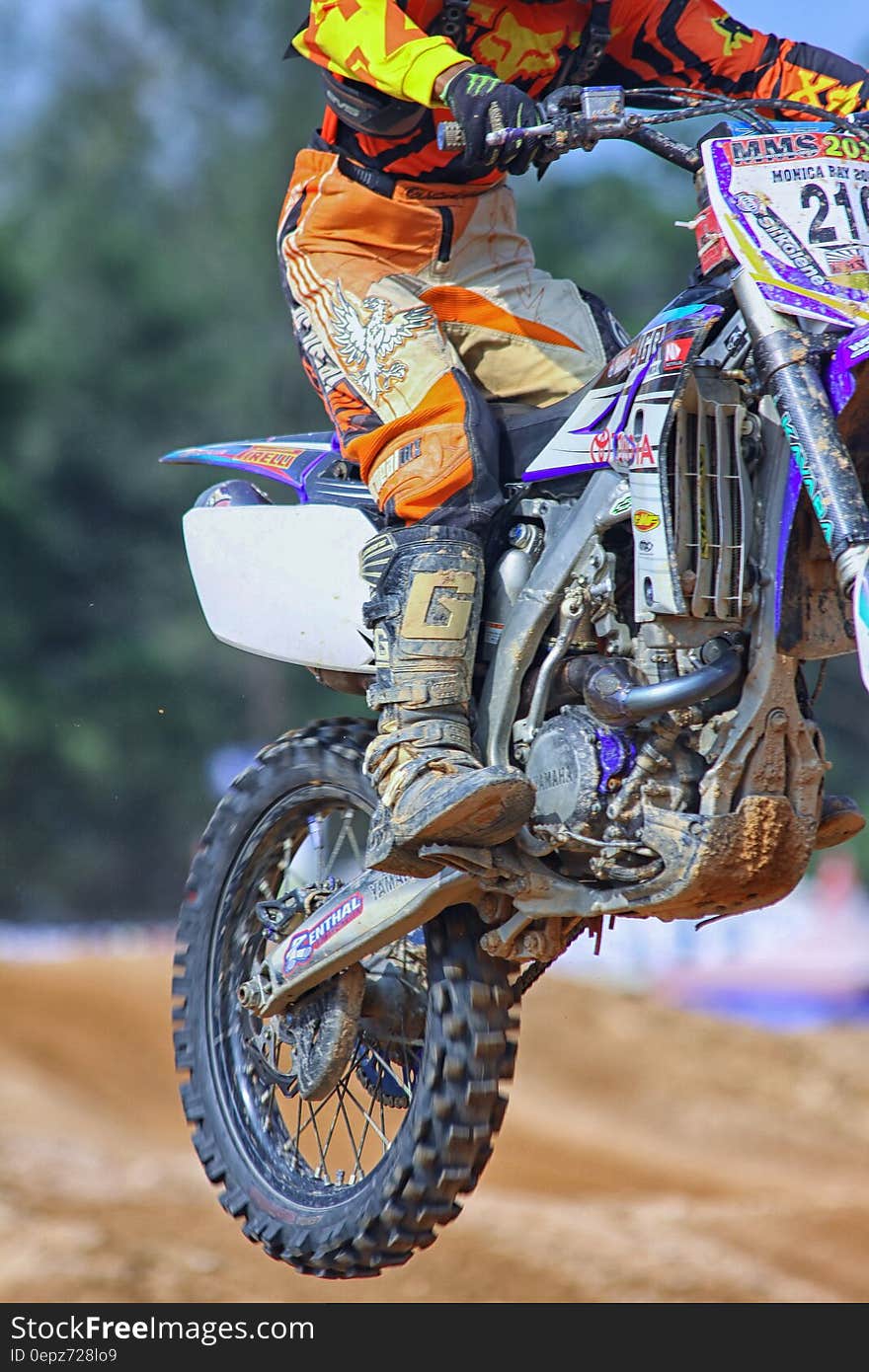 Person in Orange and Yellow Fox Motorcycle Suit Riding a Purple White Gray and Black Dirt Motorcycle Outdoors during Daytime