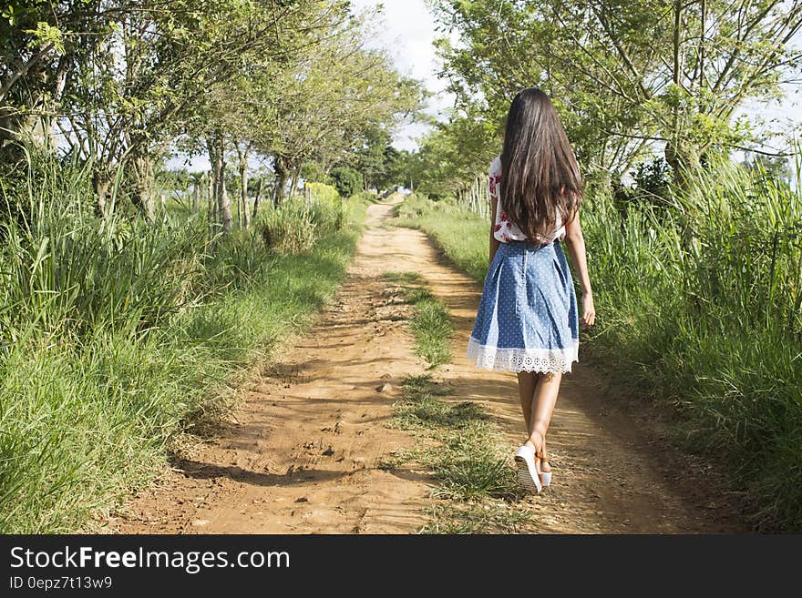 Woman Wearing Blue and White Skirt Walking Near Green Grass during Daytime