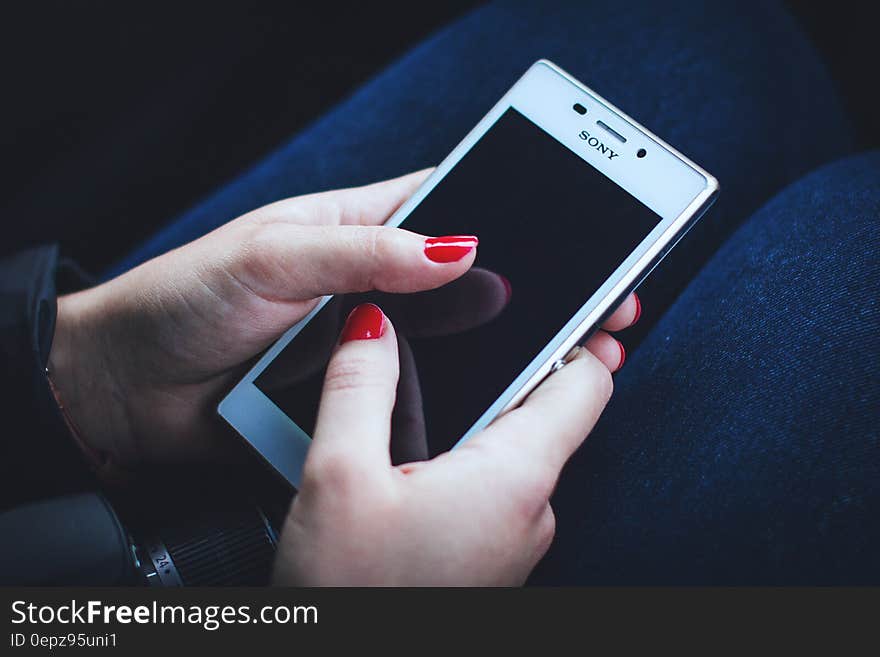 Close up of woman with red painted nails holding Sony smartphone. Close up of woman with red painted nails holding Sony smartphone.