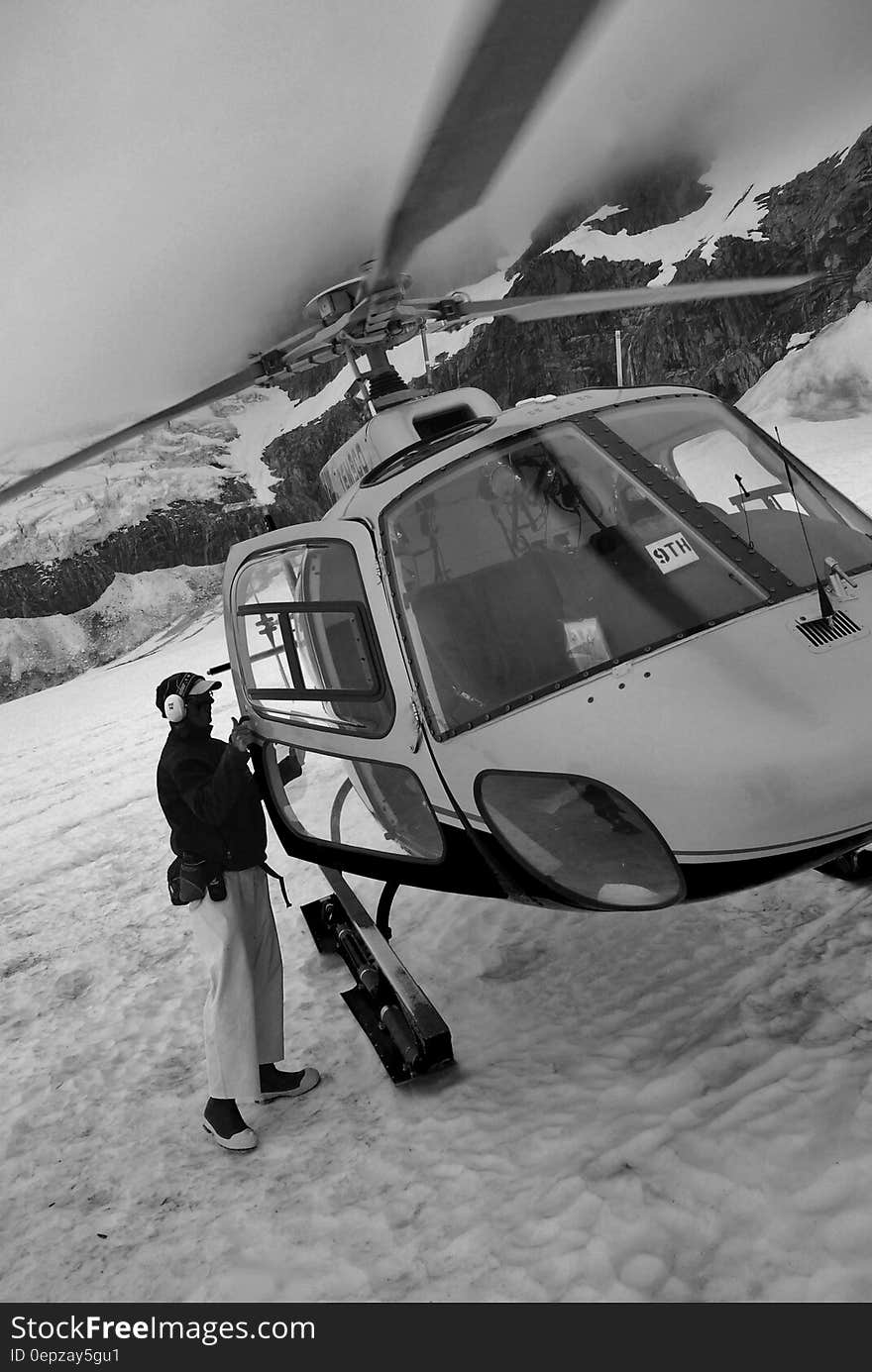 Man standing next to helicopter on snow in mountains in black and white. Man standing next to helicopter on snow in mountains in black and white.