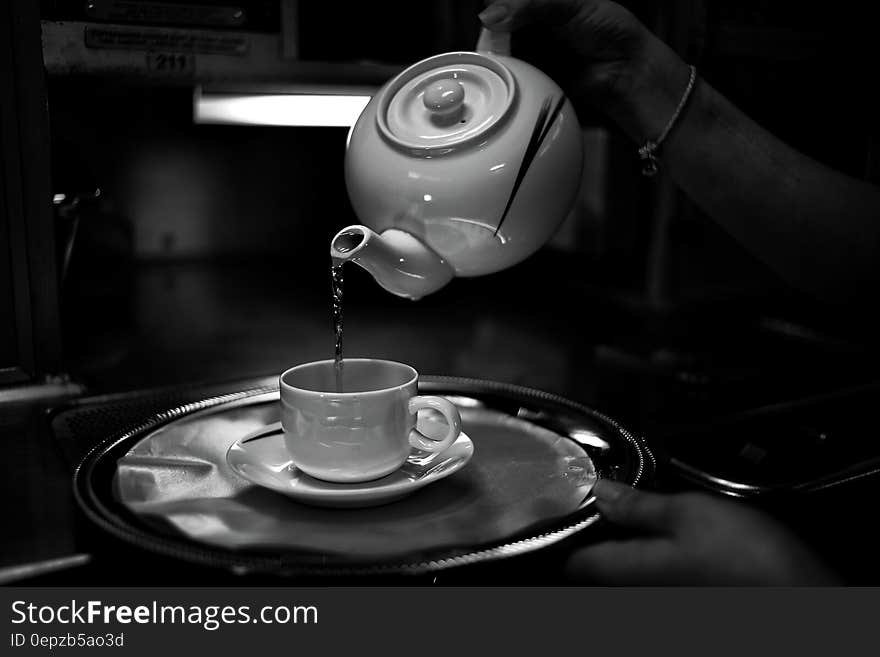 Tea pouring from china pot into cup on saucer and tray in black and white. Tea pouring from china pot into cup on saucer and tray in black and white.