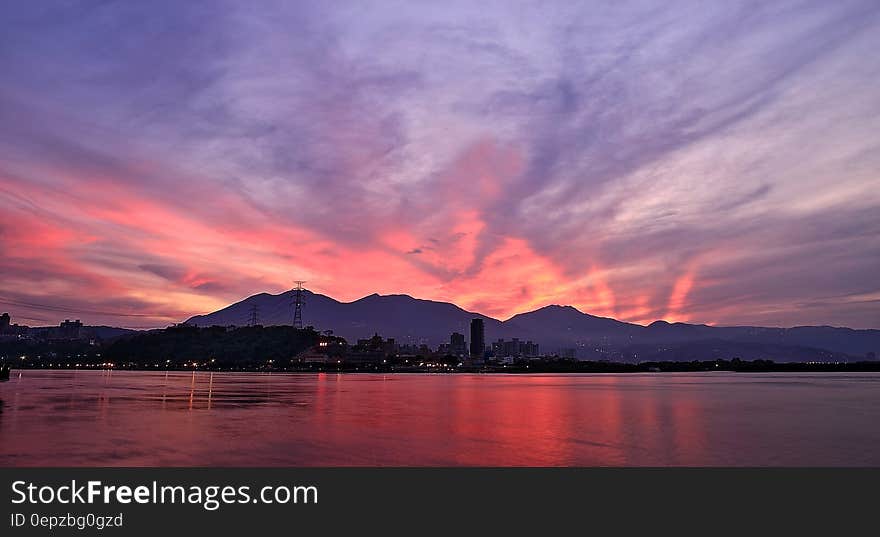 Silhouette Photo of City Buildings Near Sea With Mountain during Golden Time