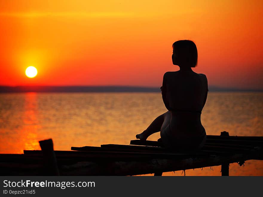 Silhouette of Woman Sitting on Dock during Sunset