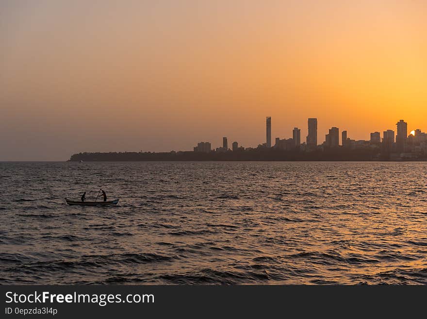 2 Person on the Boat on the Ocean in Front Urban City during Golden Hour