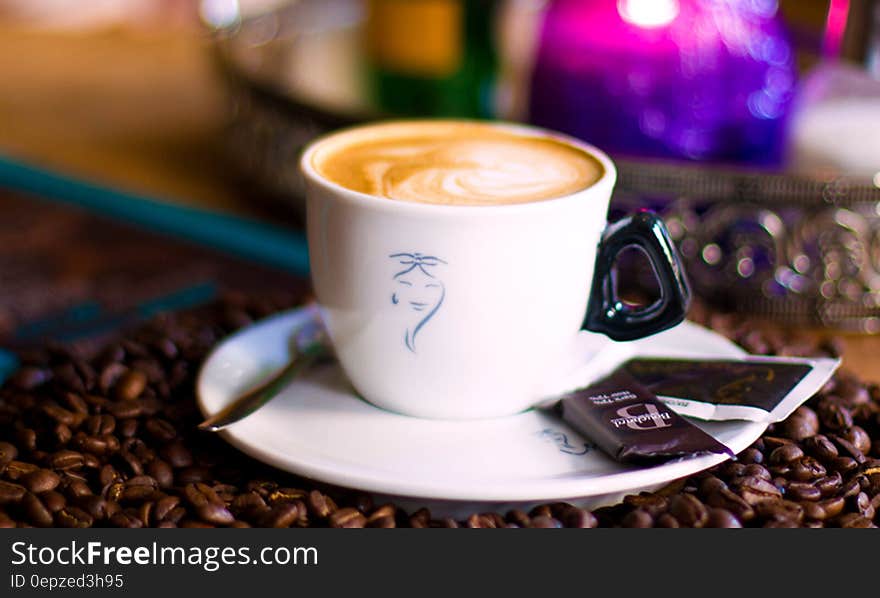 White china cup with coffee on saucer with roasted beans on wooden table. White china cup with coffee on saucer with roasted beans on wooden table.