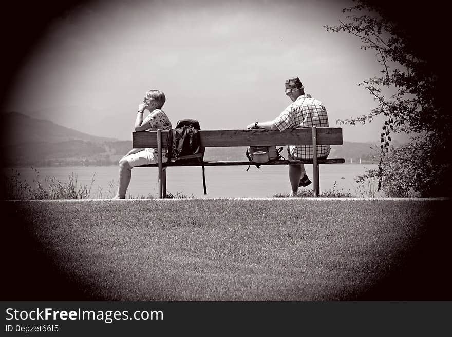 Man Sitting on Other Edge of Bench Parallel to Woman With Bags in Between Them