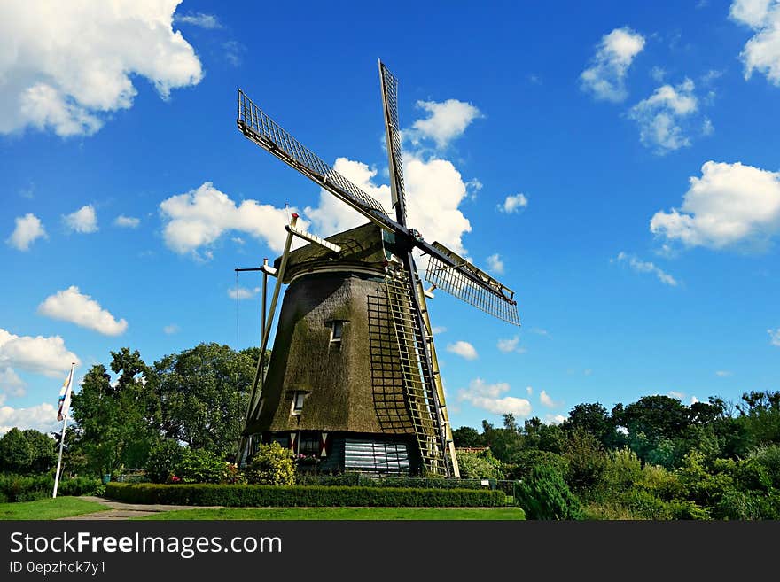 Brown and Black Windmill Under Cumulus Clouds Surrounded by Green Leaf Trees