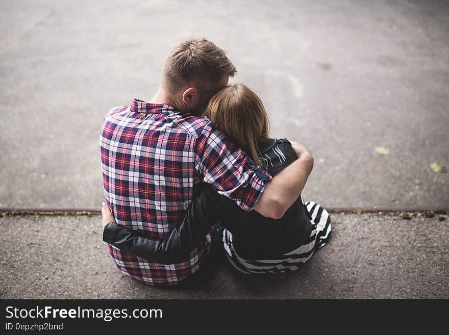 Man in Red White and Blue Check Long Sleeve Shirt Beside Woman in Black and White Stripes Shirt Hugging Each Other While Sitting o