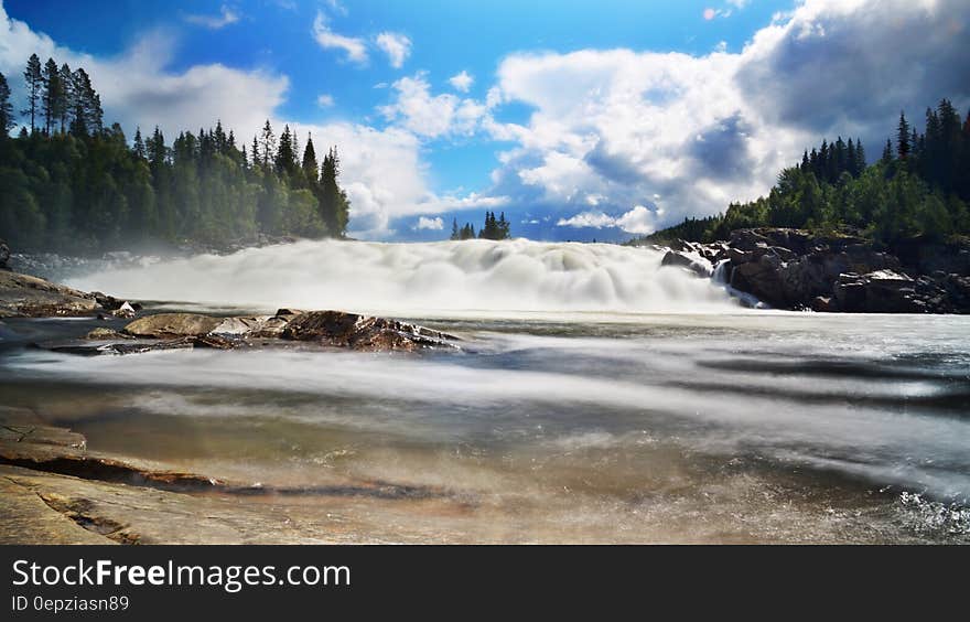 River Near Trees Under Blue Sky and White Clouds