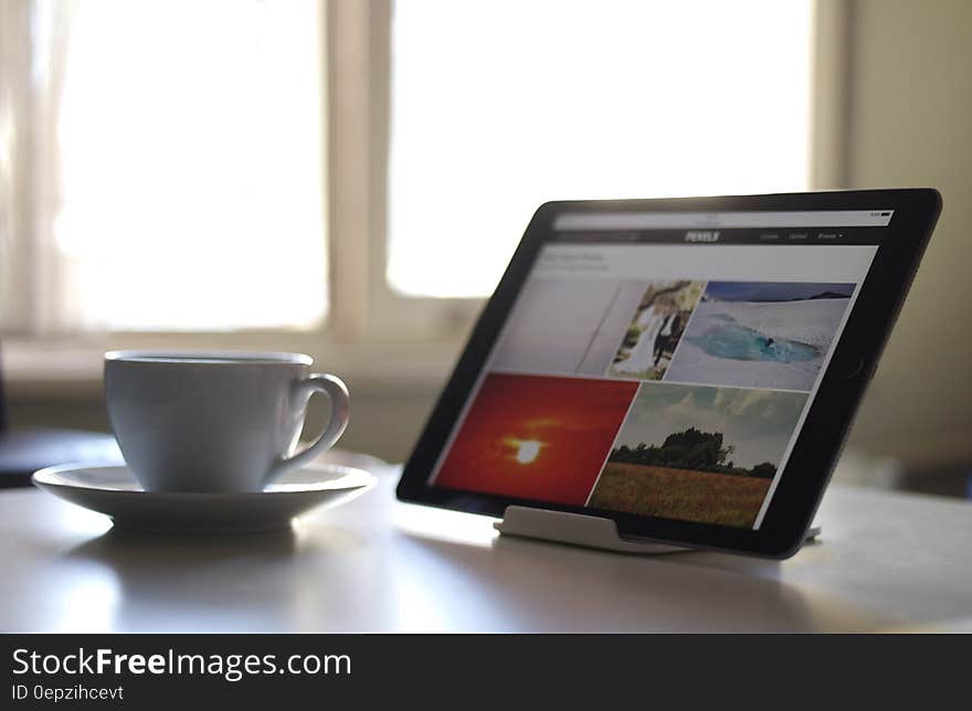 Black Tablet Computer Near a White Ceramic Teacup