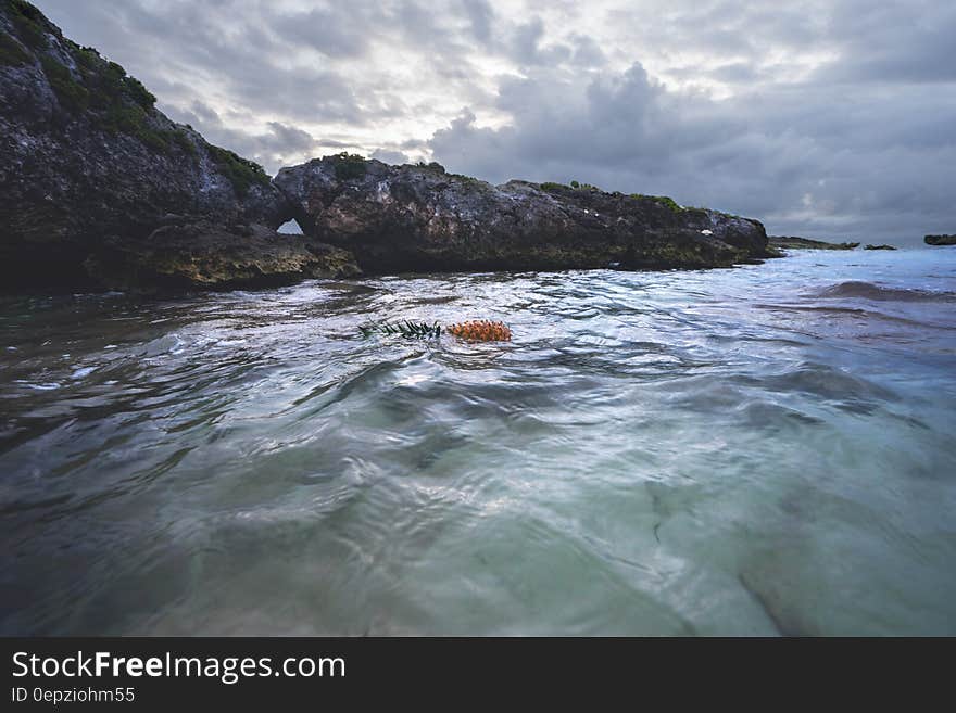 Rocky Cliff Near Calm Sea Under Gray Cloudy Sky