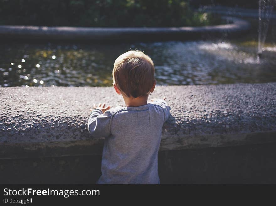 Boy in Gray Top Standing in Front of Water Fountain