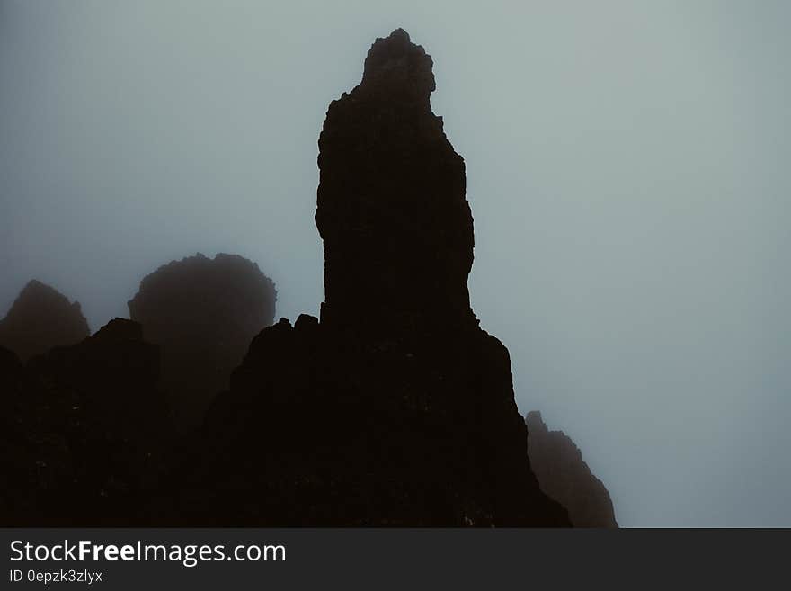 Silhouetted rock stack on misty mountainside.