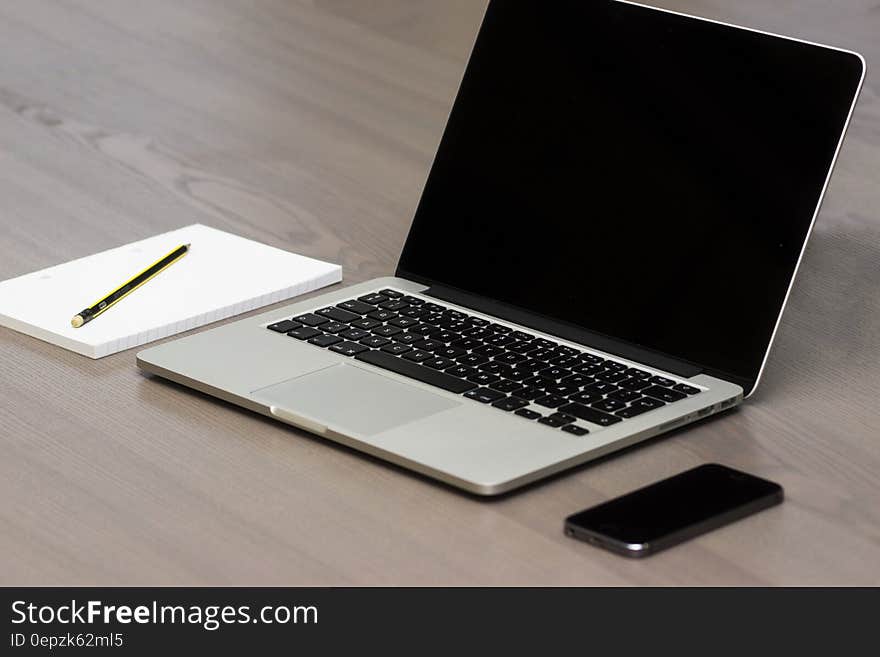 Open laptop computer and cellphone on wooden desk with pad of paper and pencil. Open laptop computer and cellphone on wooden desk with pad of paper and pencil.