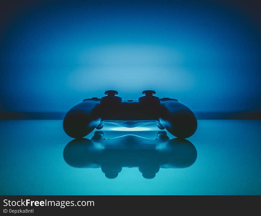 Dualshock gaming controller reflecting on blue background with copy space.