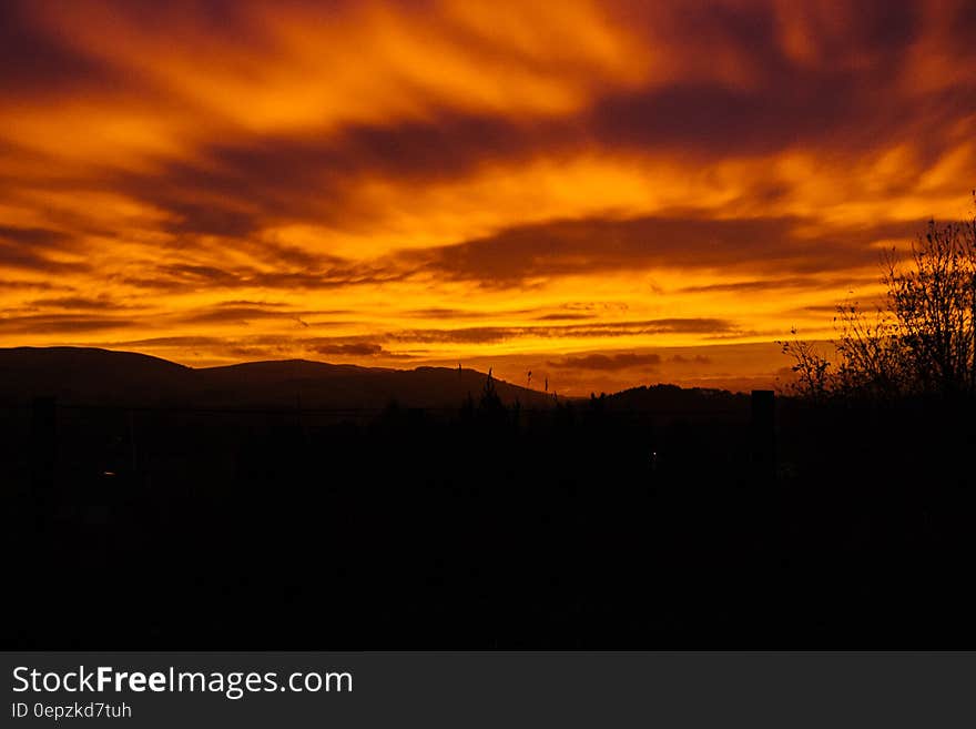 Scenic view of orange sunset and cloudscape over silhouetted countryside.