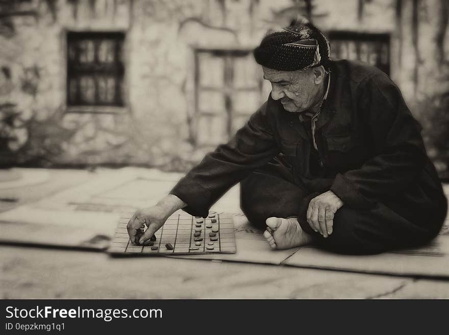 Old man with rocks on board sitting on ground in black and white. Old man with rocks on board sitting on ground in black and white.