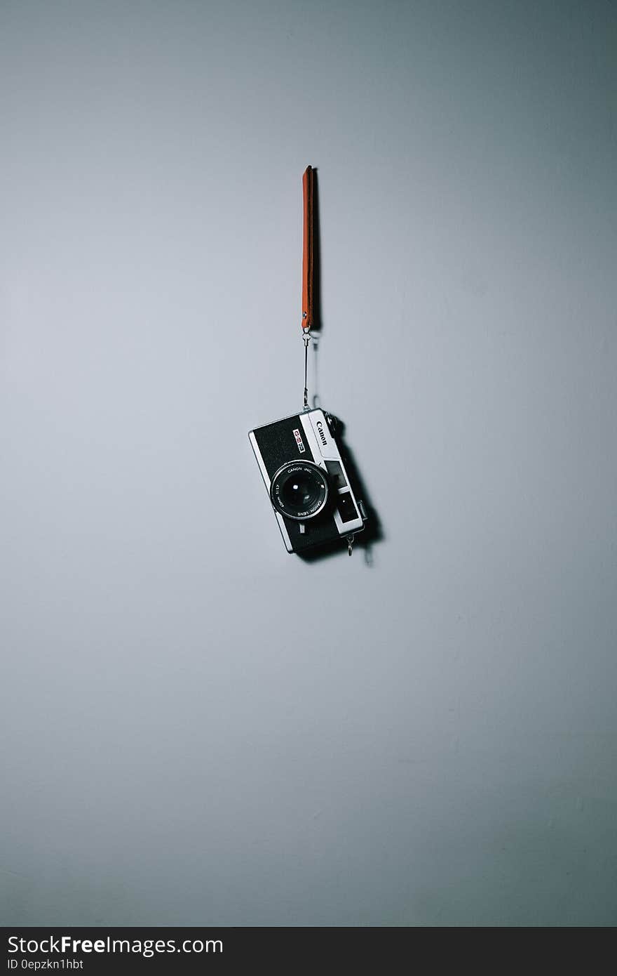 Vintage Canon camera hanging from strap on wall.