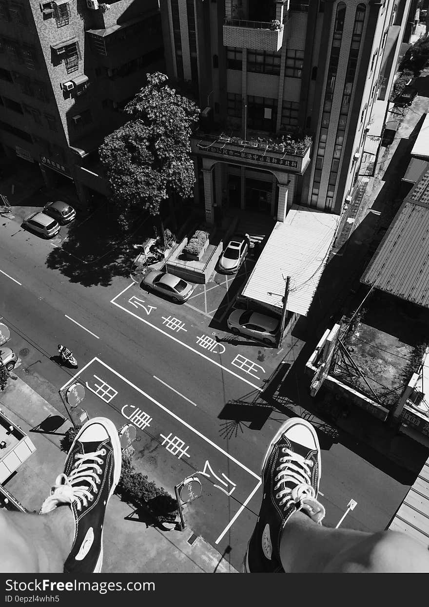 Grayscale Photography Man Wearing All Star Converse High Tops Below in Street and Building