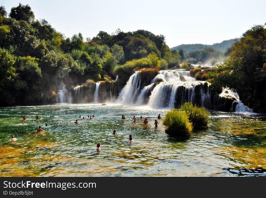 People Swimming Near Waterfall during Daytime