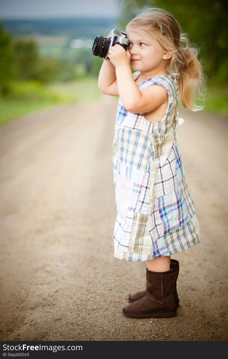 Girl With Blonde Hair and Wearing Blue and White Plaid Dress and Capturing Picture during Daytime