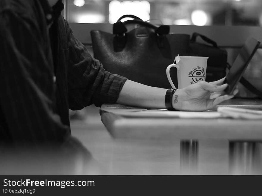 Gray Scale Photograph of Person Sitting Beside Black Leather Bag