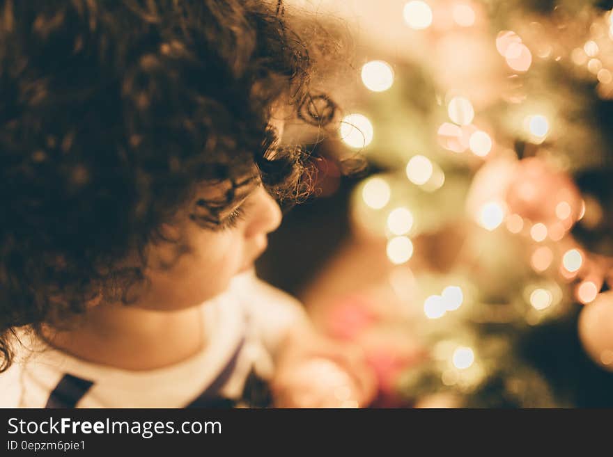 Portrait of child with brown curly hair using selective focus on one eye looking at a blur of Christmas tree lights. Portrait of child with brown curly hair using selective focus on one eye looking at a blur of Christmas tree lights.