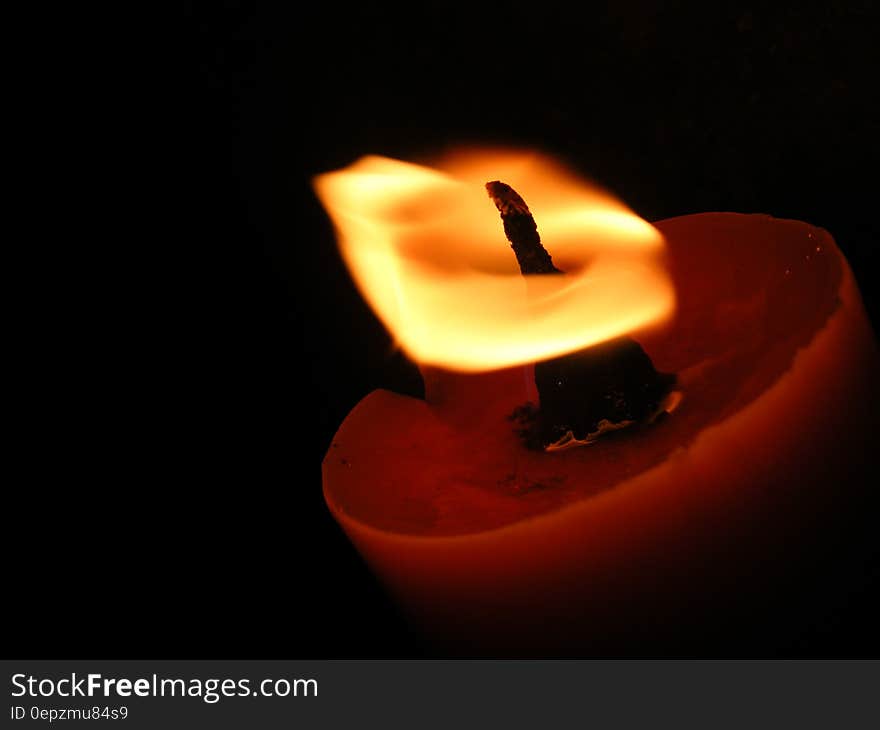 Closeup of candle burning bright in an orange saucer shaped candle holder, black background.