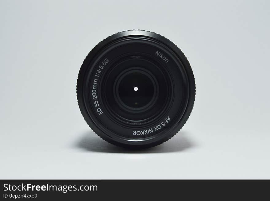 Black 55-200 mm telephoto Nikkor lens set at small aperture, white background.
