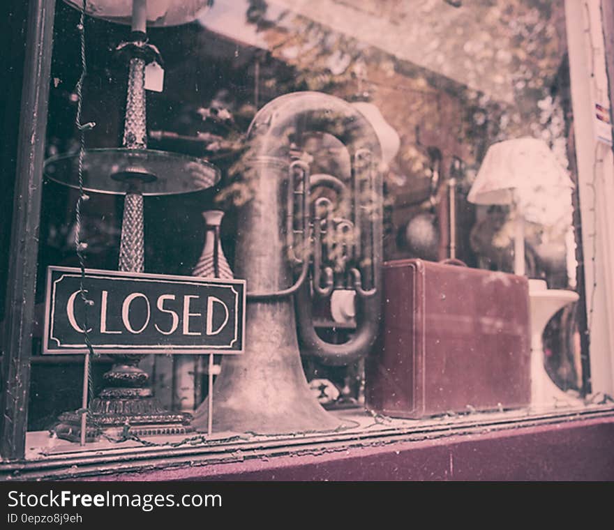 The window of an antique shop with tuba, suitcase and lamp.