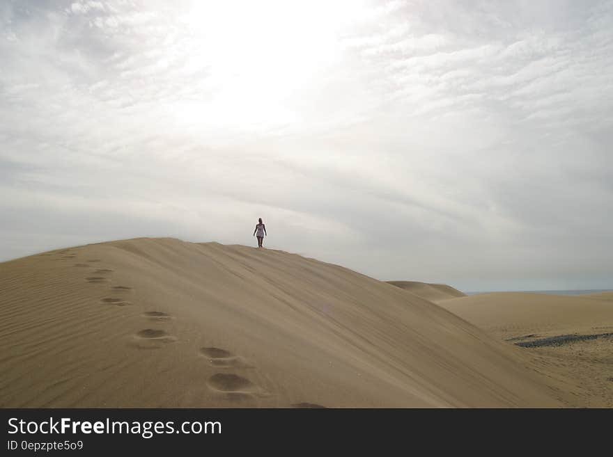 A traveler walking on sand dunes under cloudy skies. A traveler walking on sand dunes under cloudy skies.