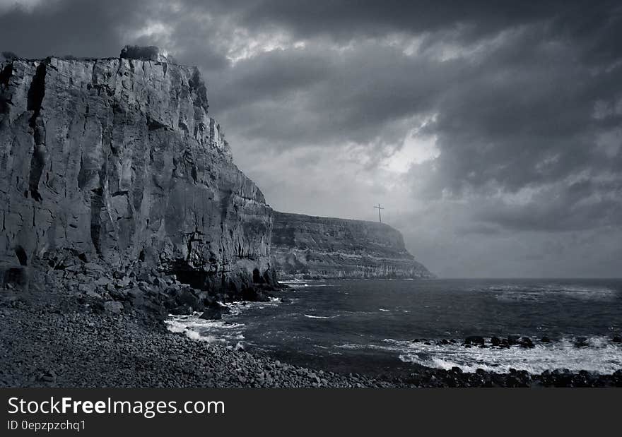 Cliff over rocky beach with waves in black and white.