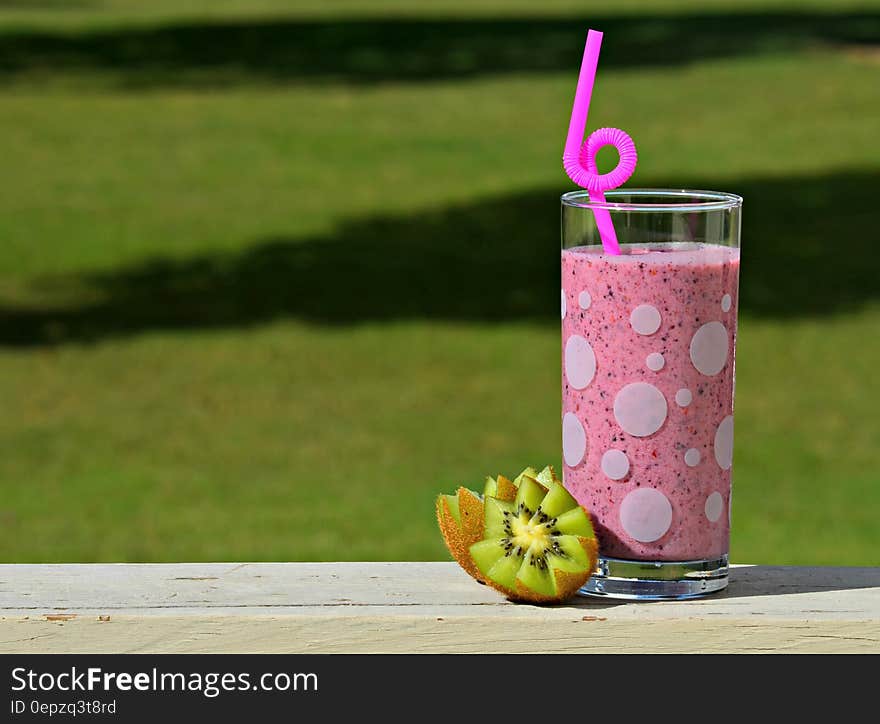 Close up of berry fruit drink in glass with straw and fresh kiwi on wooden railing outdoors on sunny day. Close up of berry fruit drink in glass with straw and fresh kiwi on wooden railing outdoors on sunny day.