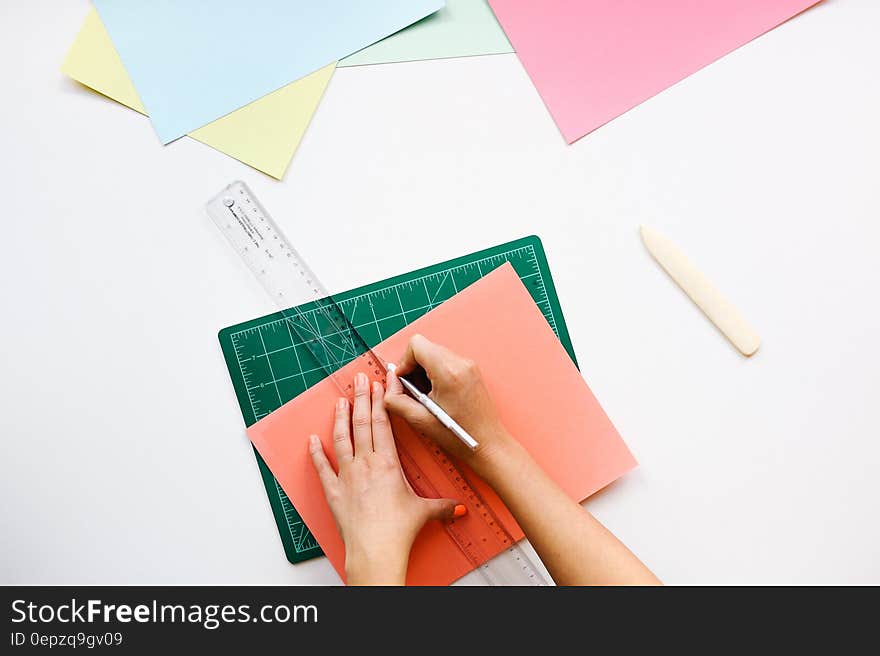 Hand using ruler and cutter on colored paper on ruled pad. Hand using ruler and cutter on colored paper on ruled pad.