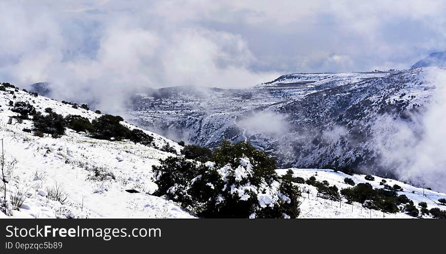 Fog over mountain peaks with snowy slopes on sunny day.