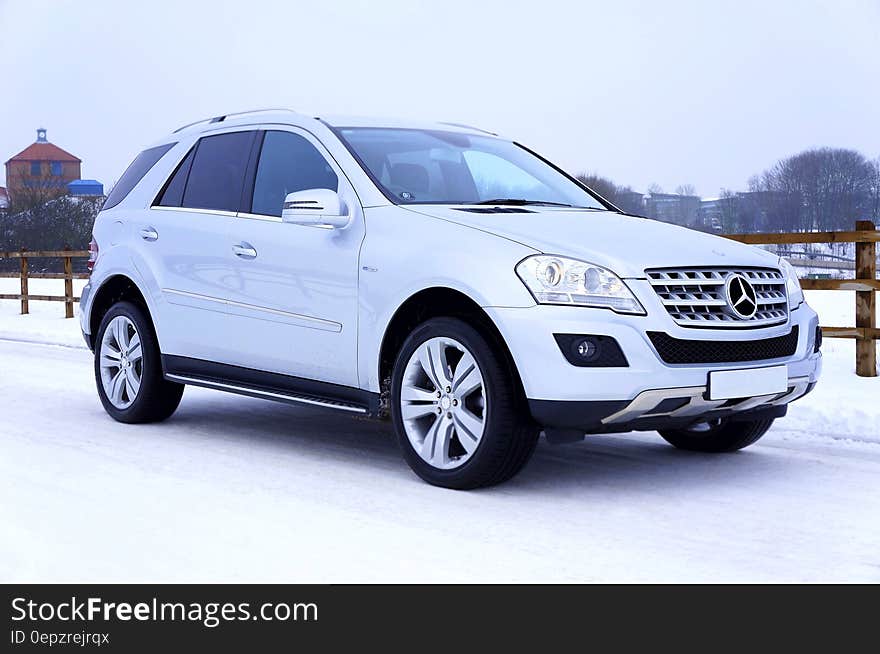 White Mercedes Benz SUV on snow covered roadway on sunny day.