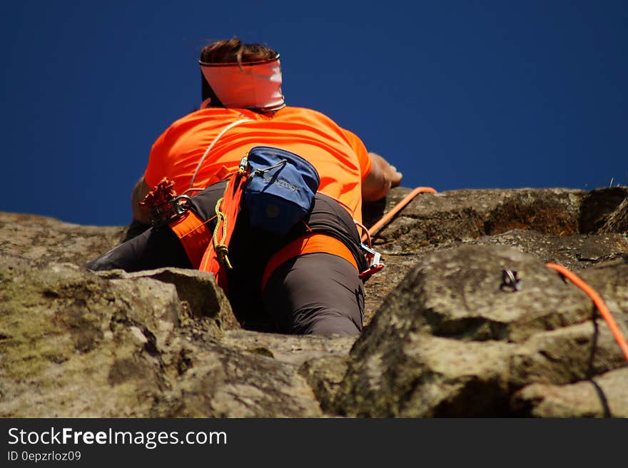 Person in Orange Shirt Climbing Rock during Daytime