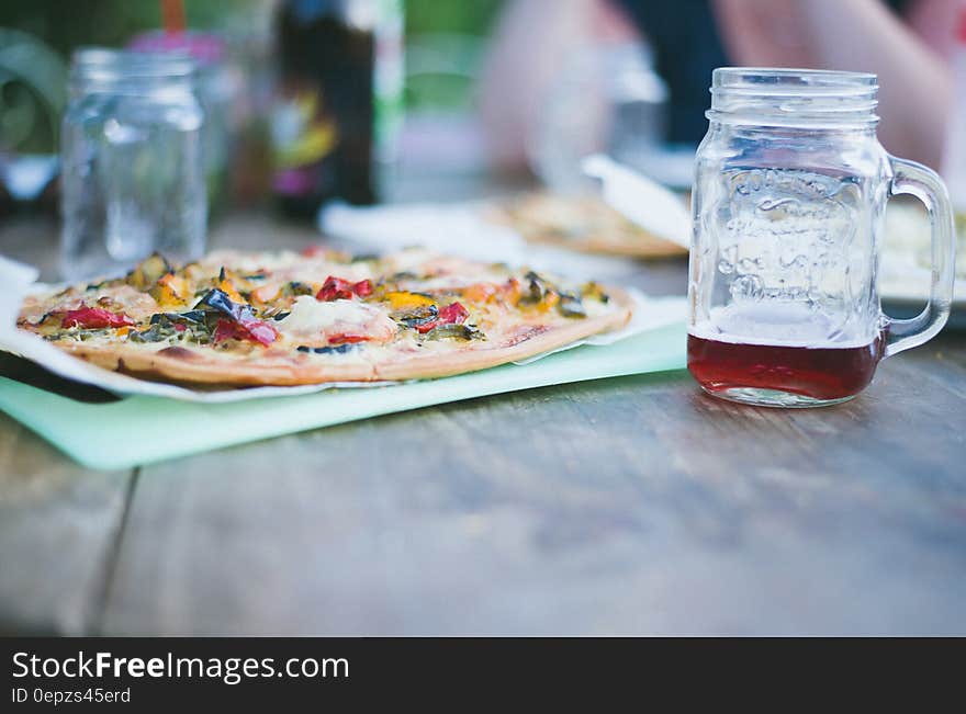 Whole pizza on cutting board with glass mason jars of tea on wooden table. Whole pizza on cutting board with glass mason jars of tea on wooden table.