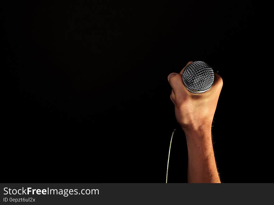 Close up of hand holding silver microphone on black with copy space. Close up of hand holding silver microphone on black with copy space.