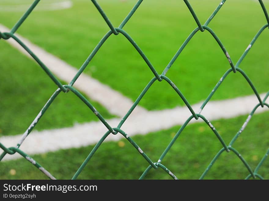 Close up of metal mesh fence around sports field on sunny day.