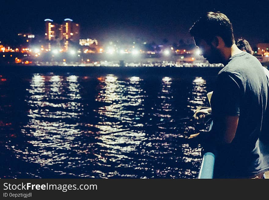 Man on waterfront fishing at night with illuminated skyline. Man on waterfront fishing at night with illuminated skyline.