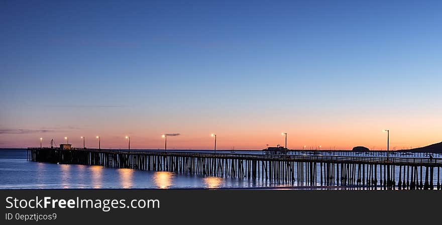 Sunset over ocean pier illuminated with streetlights.