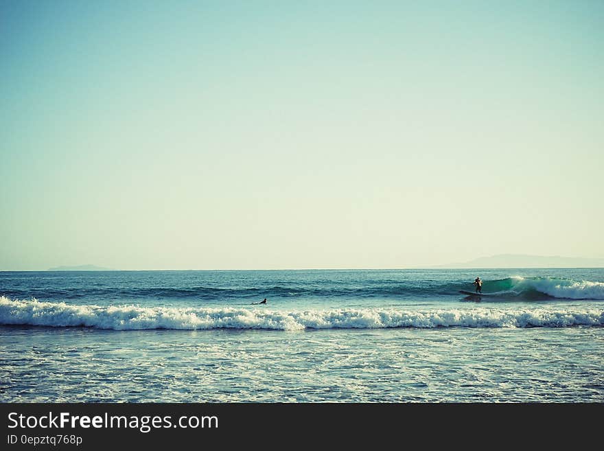 Surfer riding wave on ocean along seashore on sunny day. Surfer riding wave on ocean along seashore on sunny day.