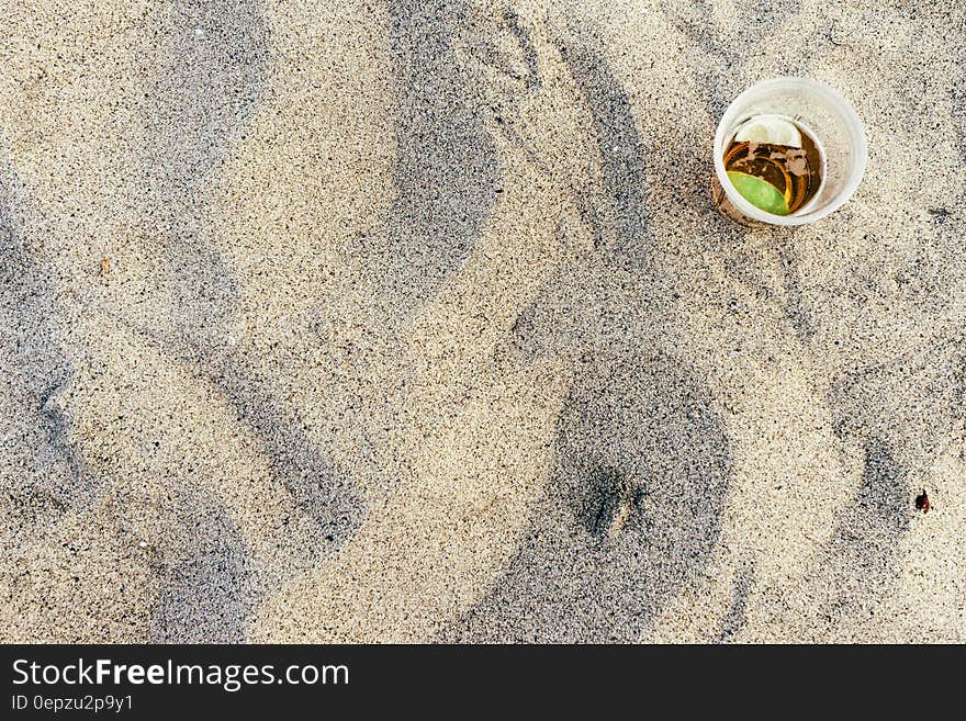 Overhead on plastic cup with drink on sandy beach on sunny day.